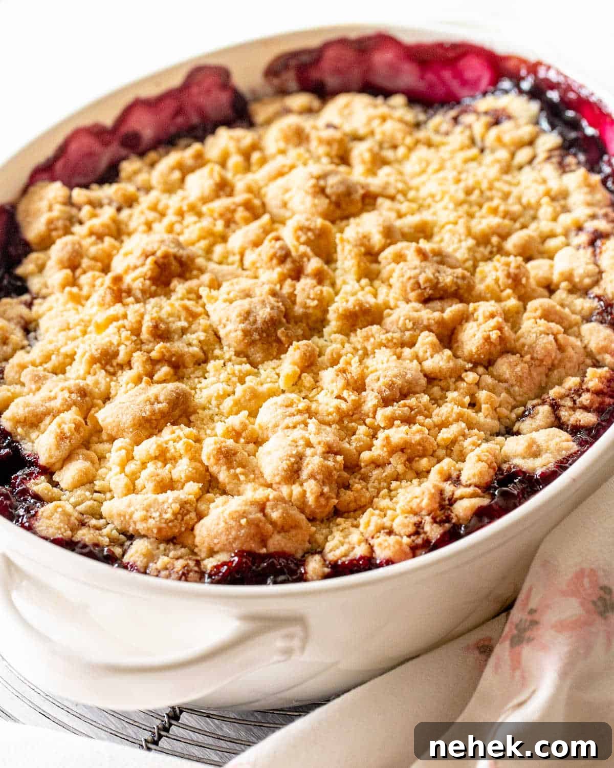 Baked cherry dump cake in oval white dish, white background, pink and white linen.