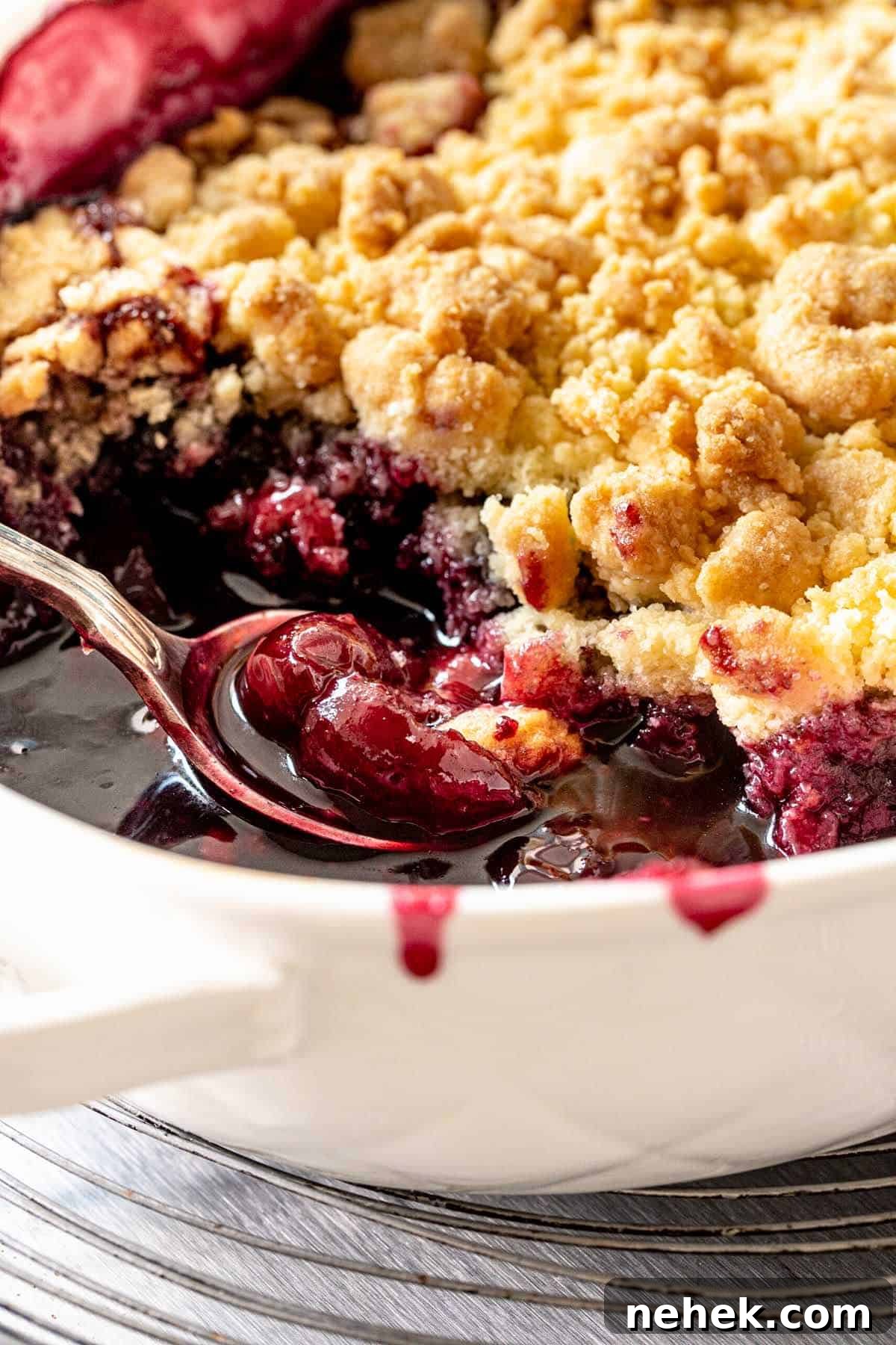 Spoon inside white dish with cherry dump cake on a wire rack.