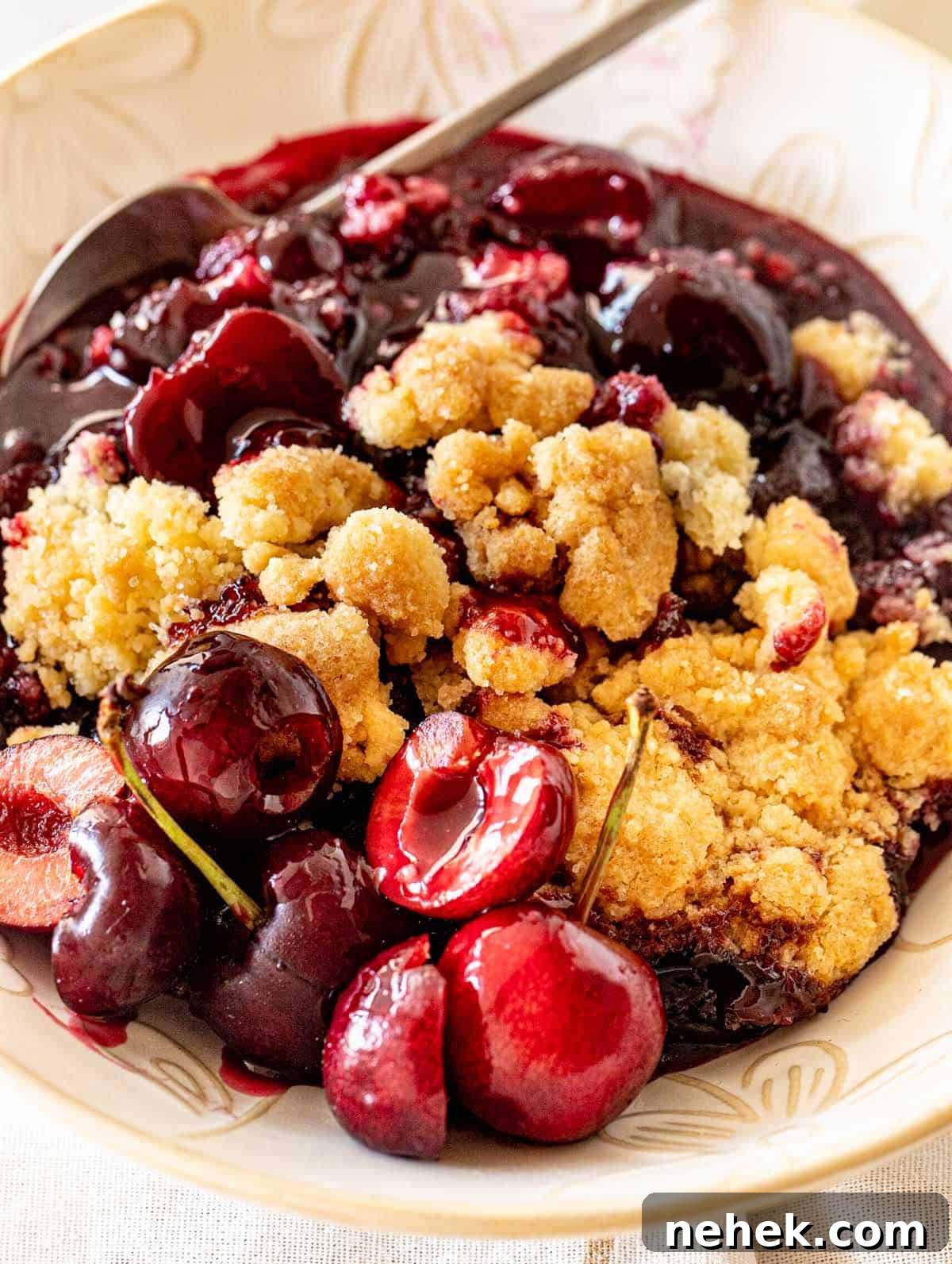 Serving of cherry dump cake on white bowl with silver spoon.