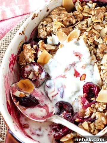 White individual dish with cherry crisp, silver spoon and melted ice cream, rustic background.