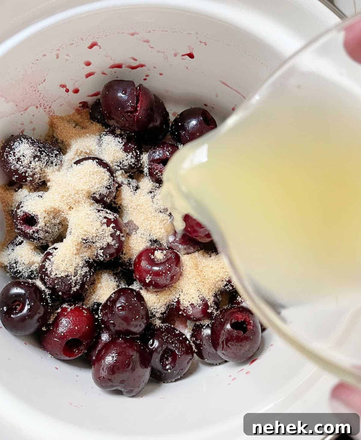 Pouring lemon juice onto cherries and brown sugar in white saucepan.
