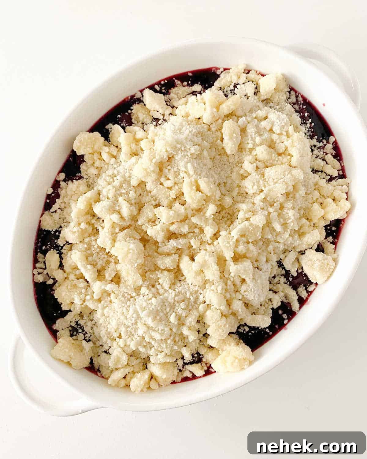 Unbaked cherry dump cake in oval white dish on white surface, top view.