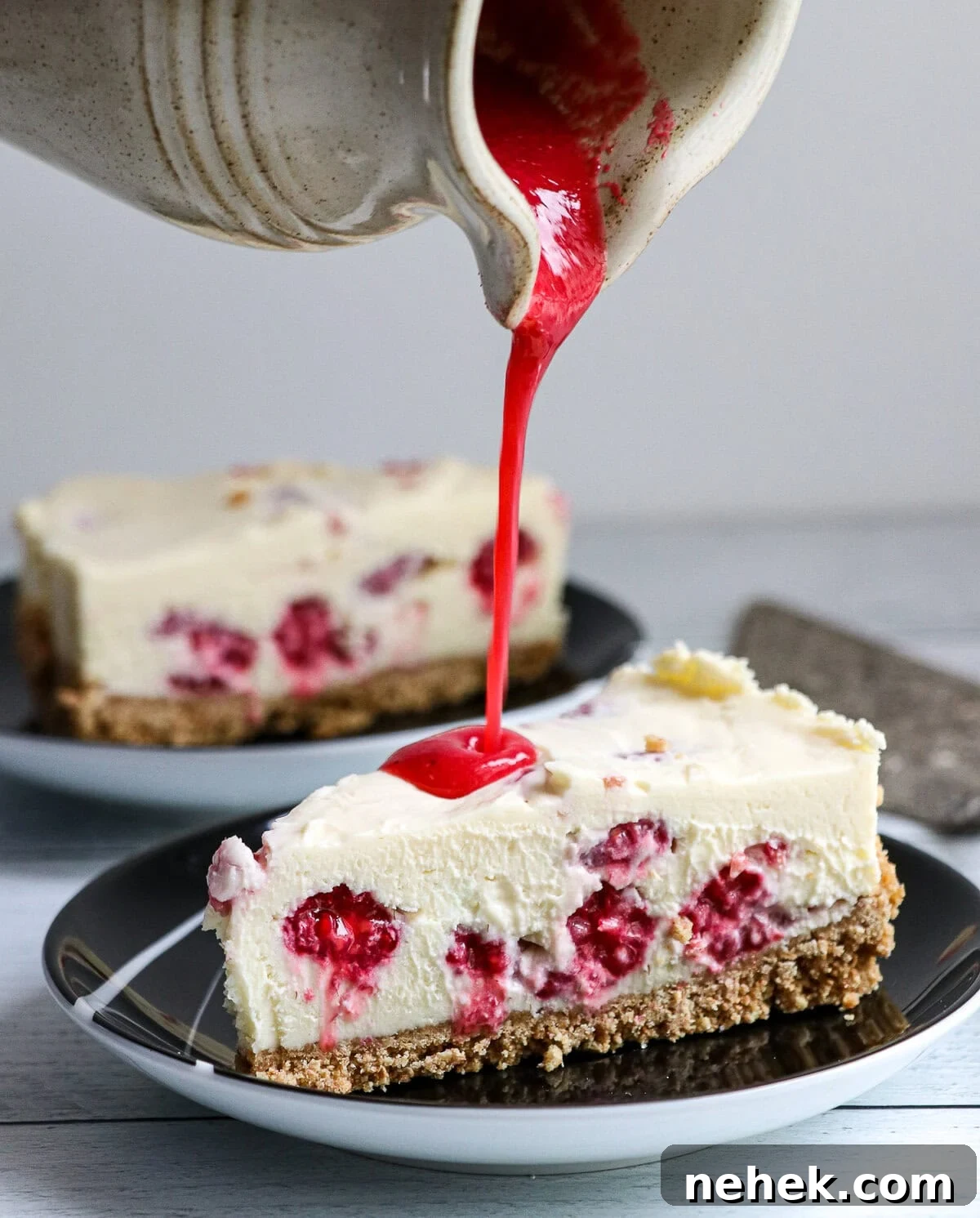 raspberry coulis being poured on cheesecake