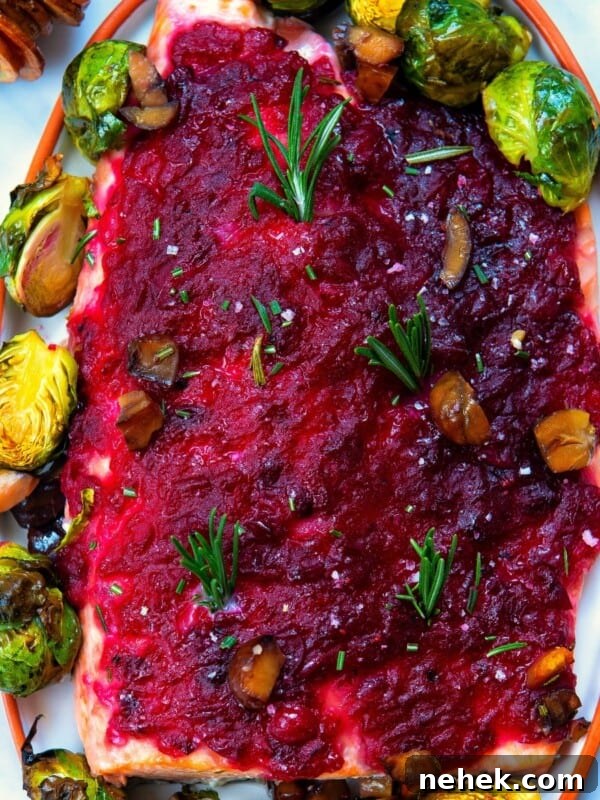 baked christmas salmon served with cranberry sauce an brussels sprouts on a white plate.