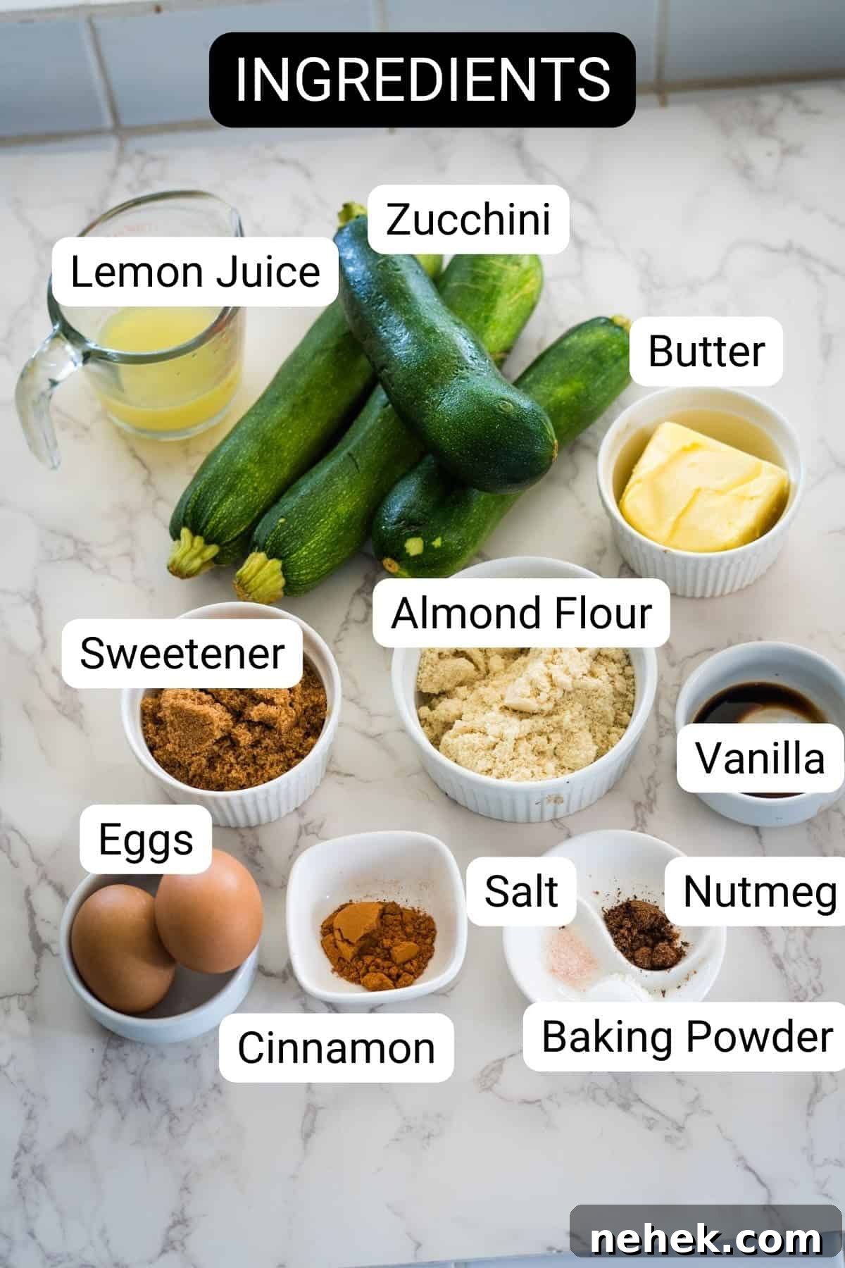Ingredients for a zucchini recipe are arranged on a marble countertop: zucchini, butter, lemon juice, almond flour, sweetener, vanilla, eggs, salt, nutmeg, baking powder, and cinnamon.