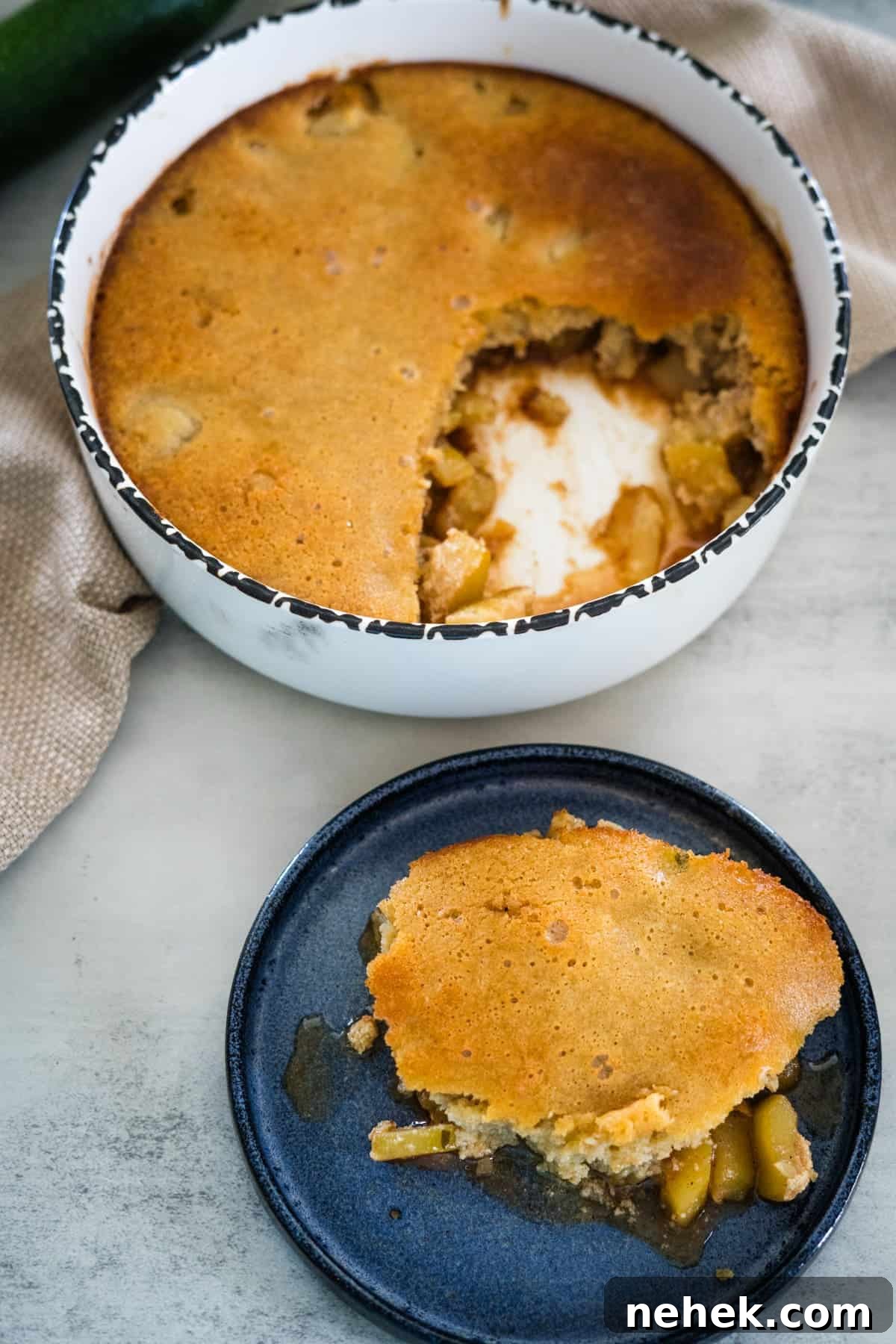 A round baking dish filled with a partially eaten golden brown cobbler and a separate serving on a dark plate, showing fruit filling inside.