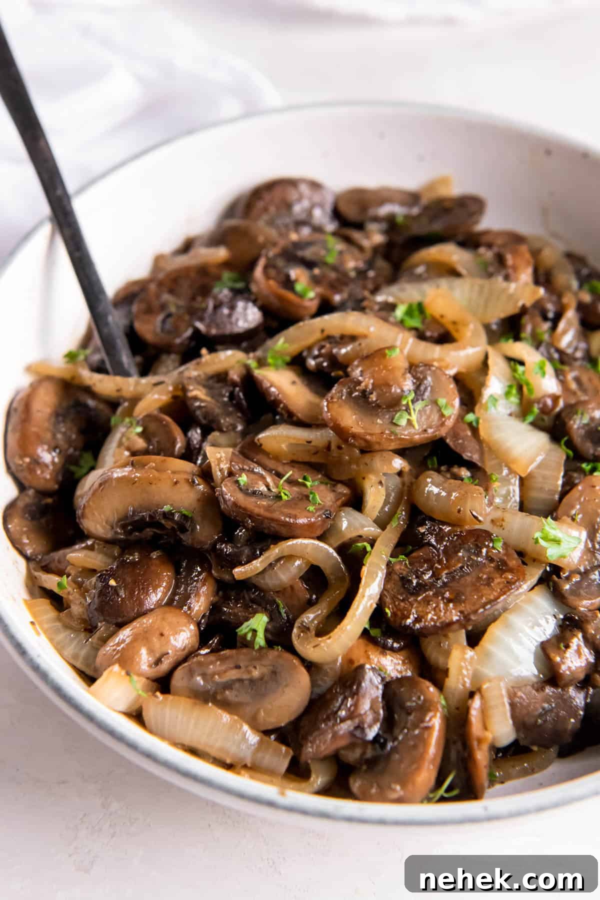 Sautéed mushrooms and onions in a white bowl on a white tabletop.