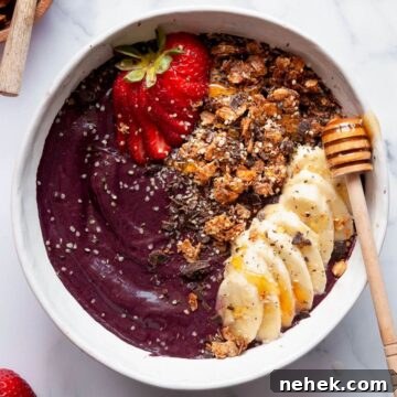 Healthy, high protein acai bowl topped with fresh strawberries, granola, sliced banana, chia seeds, and a drizzle of honey.