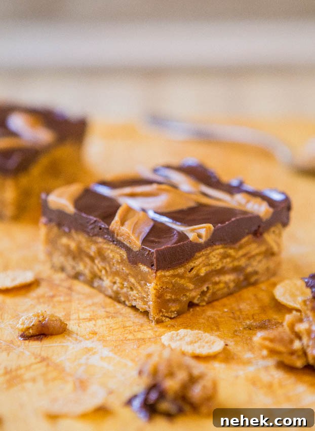Peanut butter chocolate bars with a drizzle on a wooden surface with crumbs.
