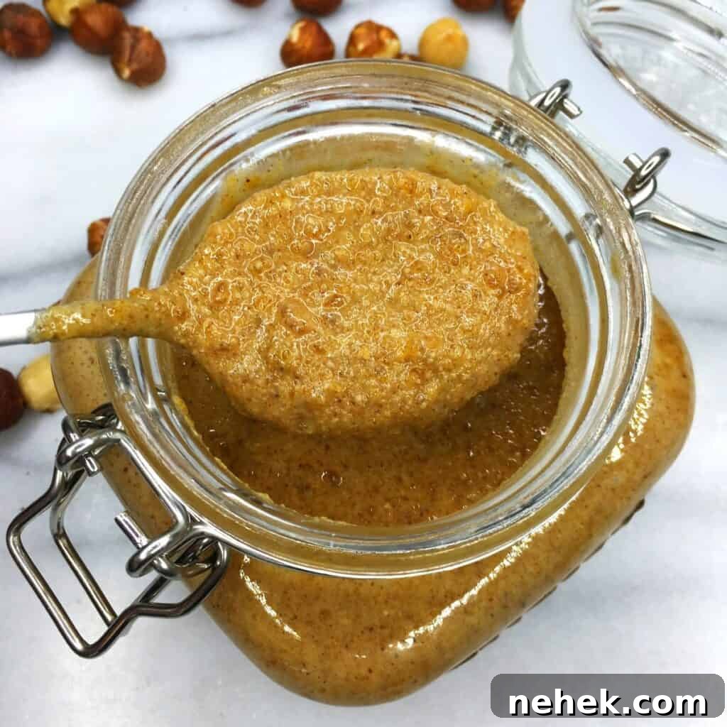A mason jar and a teaspoon over with hazelnut praline on a marble board