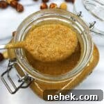 A mason jar and a teaspoon over with hazelnut praline on a marble board.