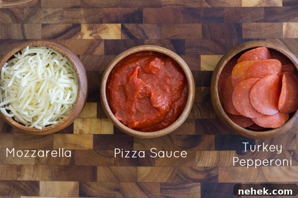 A bowl of mozzarella cheese, a bowl of pizza sauce, and a bowl of turkey pepperoni all sitting on a cutting board.