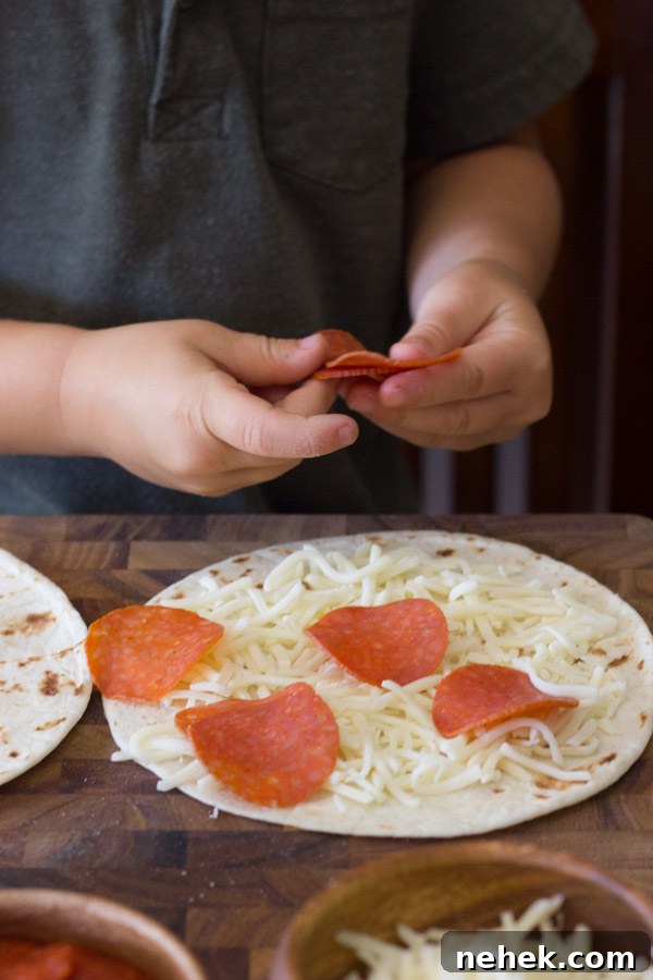 A tortilla with cheese and pepperoni on it, with more pepperoni being placed on it by a child.