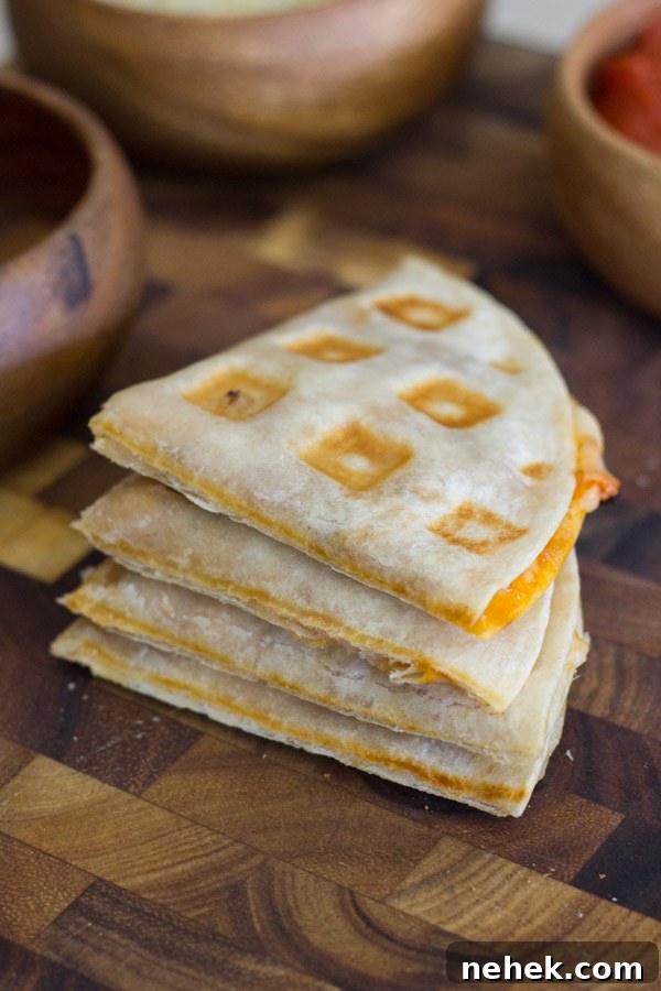 Waffled Pizza Pocket cut in four pieces and stacked in a pile on a cutting board, with bowls of ingredients in the background.
