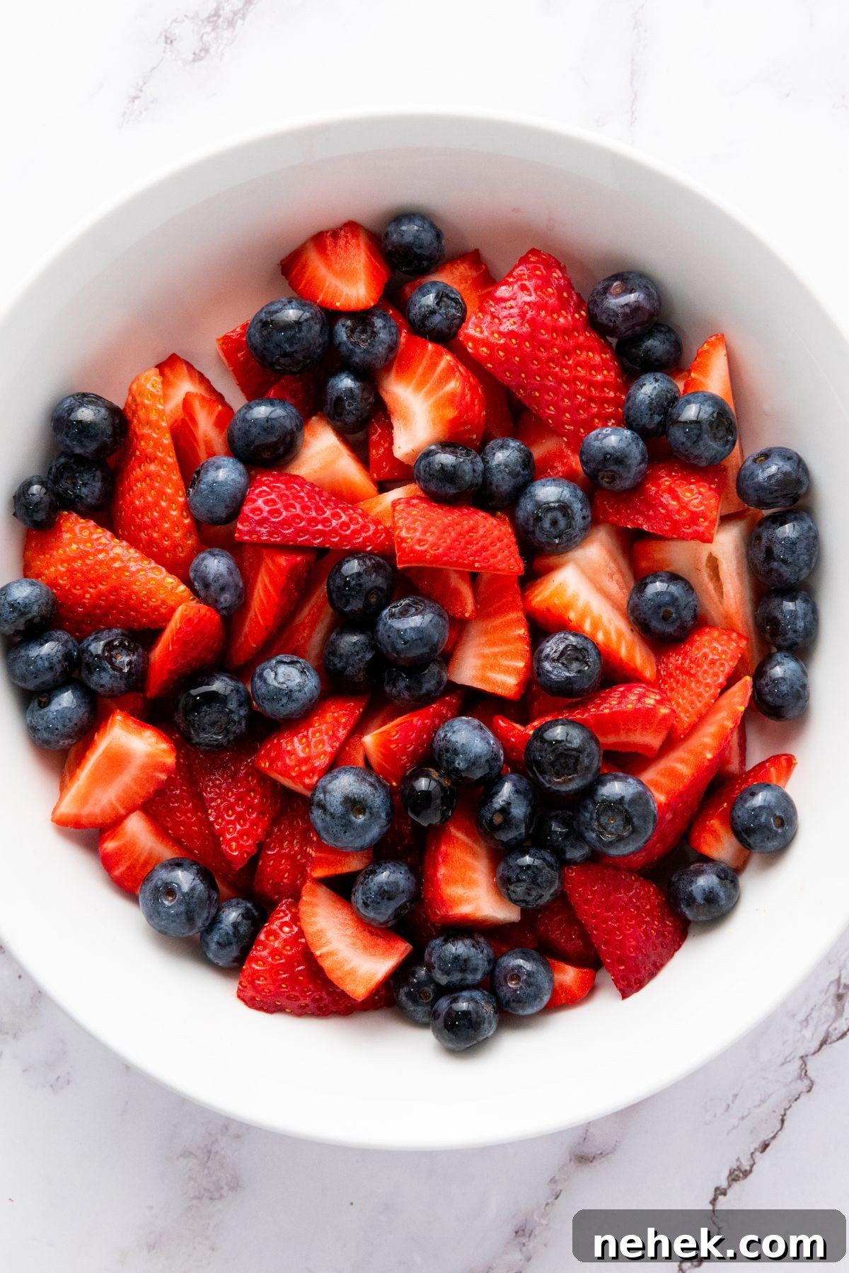 A bowl of fresh sliced strawberries and blueberries.