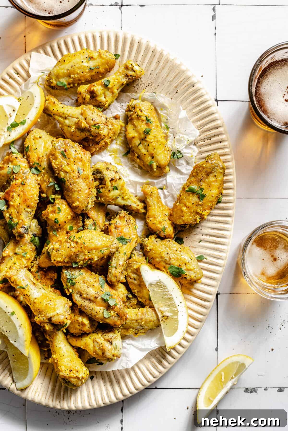Lemon Pepper Baked Chicken Wings on platter. Beer in glasses surrounding platter.