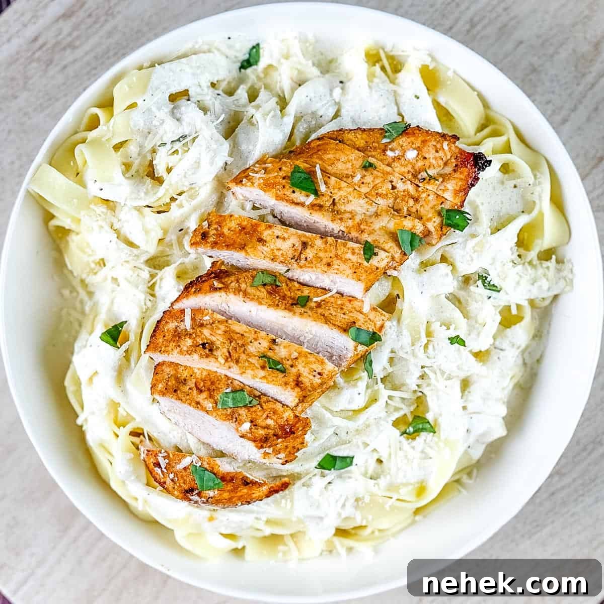 A chicken breast placed on top of noodles tossed with creamy sauce.