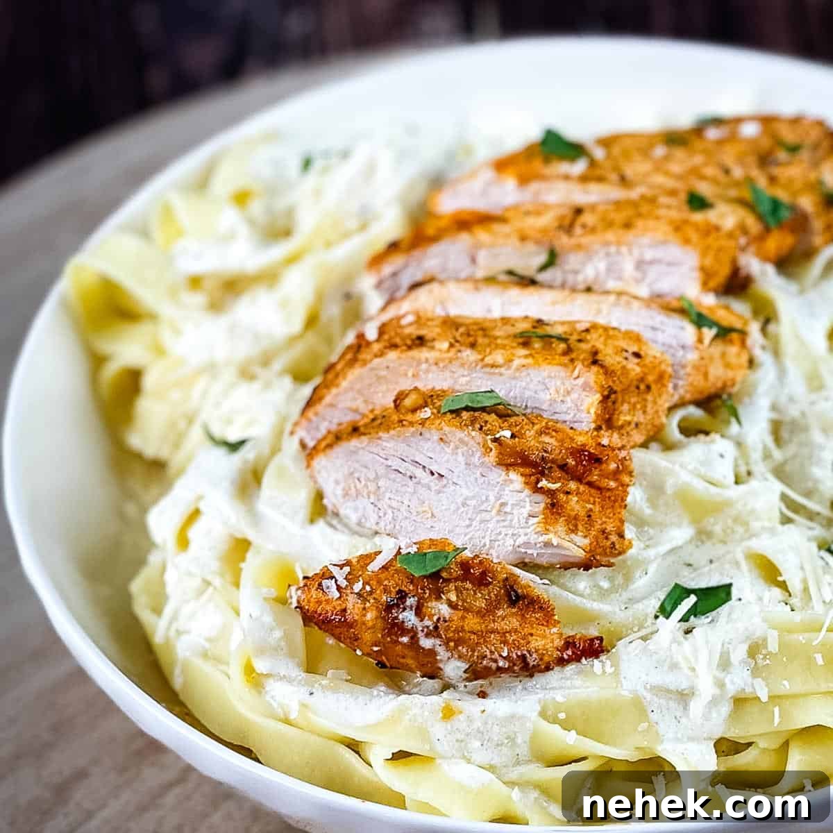 A pasta bowl filled with chicken alfredo garnished with herbs.