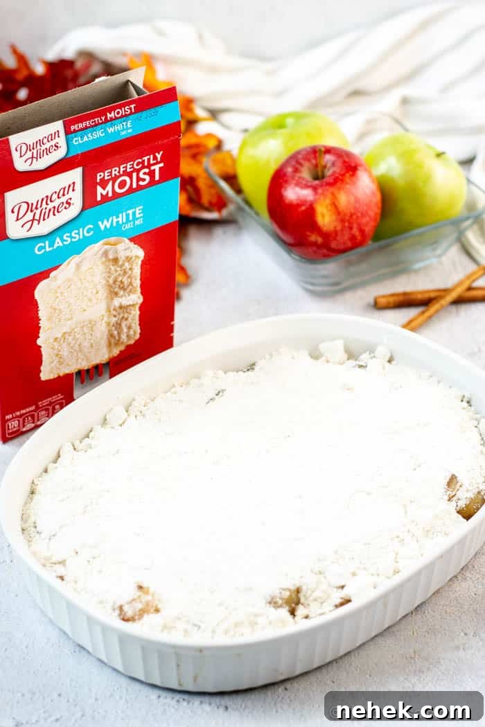 Caramel Apple Dump Cake Recipe with Homemade Sauce 5 White baking dish with 2nd layer of dry whit cake mix poured over the top of the Apple pie filling for the apple pie dump cake.