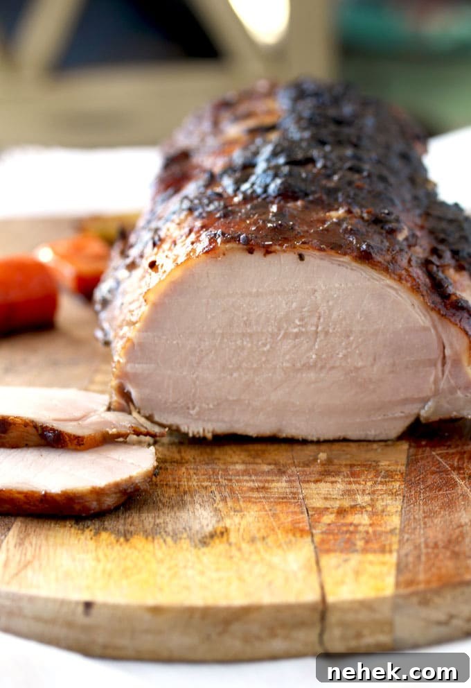 Close up view of the Oven Roasted Pork Loin on a cutting board. The roast has been sliced and you can see 2 slices laying on the side of the roast