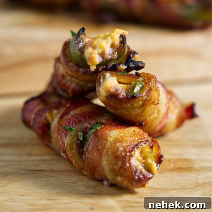 Stacked jalapeño poppers on a cutting board, wrapped in crispy bacon.