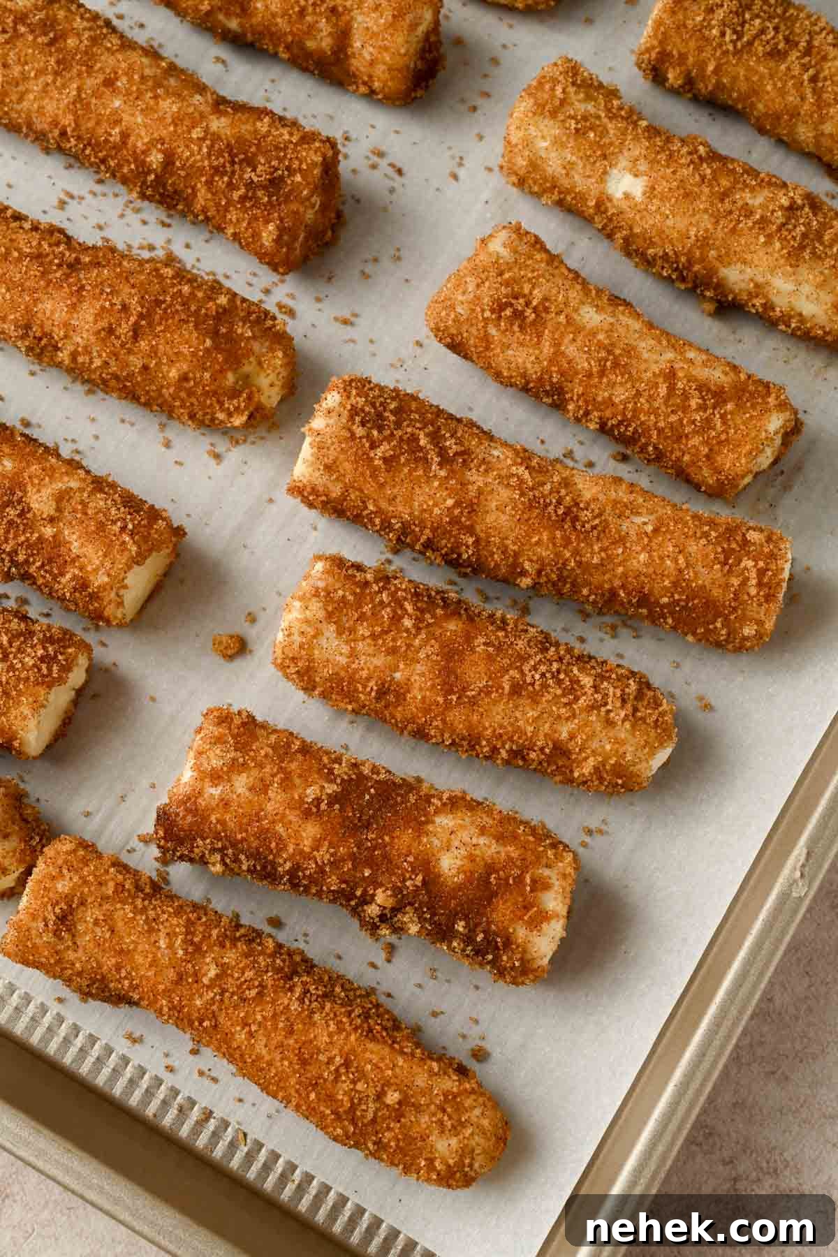 unbaked breadsticks rolled in cinnamon sugar on a parchment lined baking sheet.