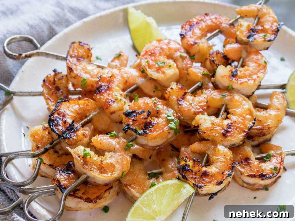 A pile of grilled margarita shrimp skewers on a white plate with lime wedges