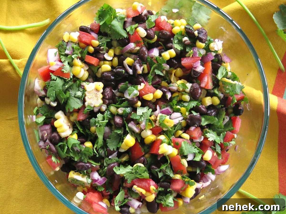 Corn and black bean salsa in a large gass bowl with a yellow napkin behind it.