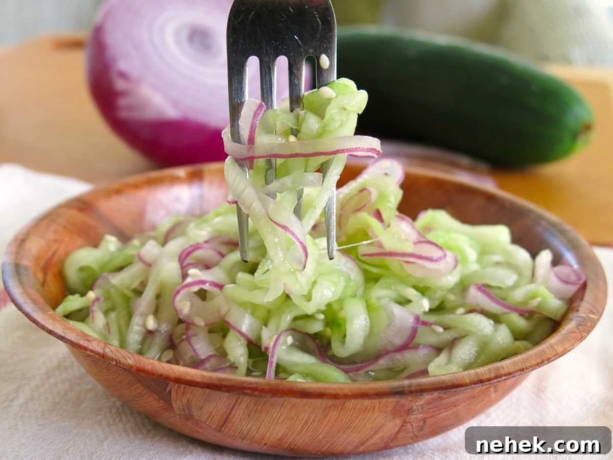 Fork lifting spiralized cucumber onion salad out of a brown bowl.