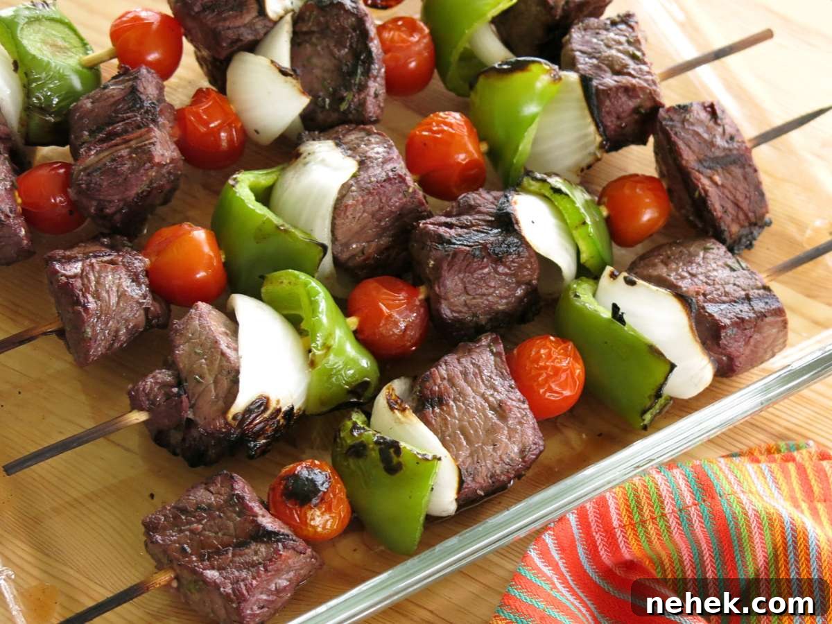 Four skewers of steak shish kebobs with tomatoes, onions, and green pepper.