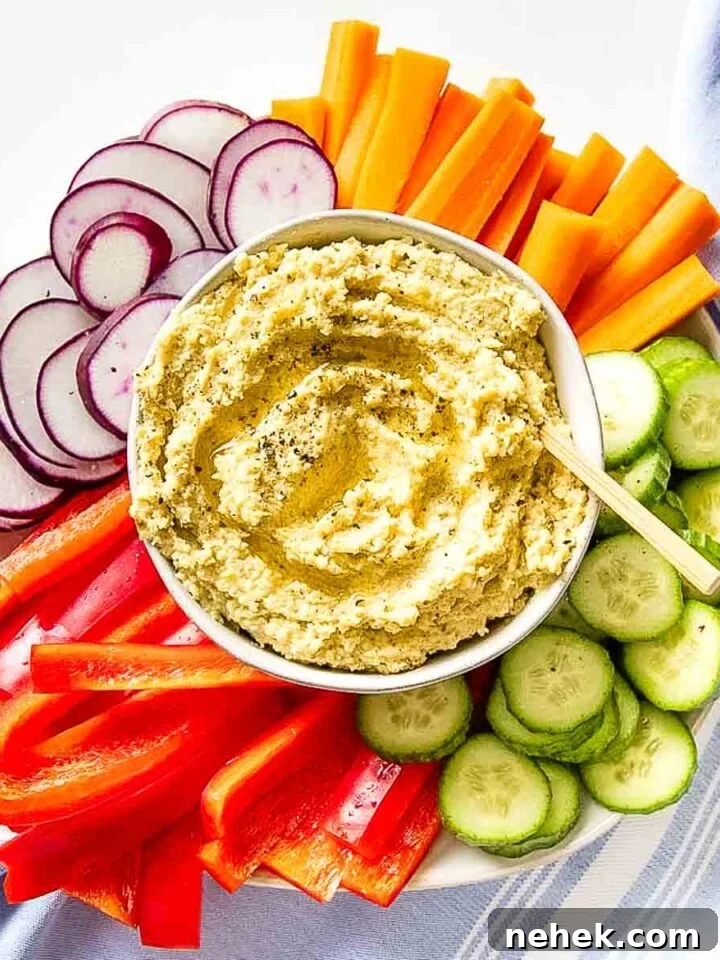 Bowl of hummus surrounded by colorful sliced veggies.