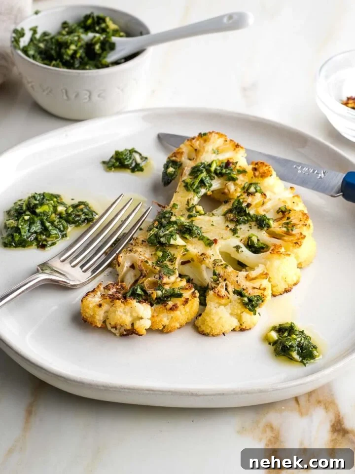 Cauliflower steak on a plate with bright green chimichurri sauce.