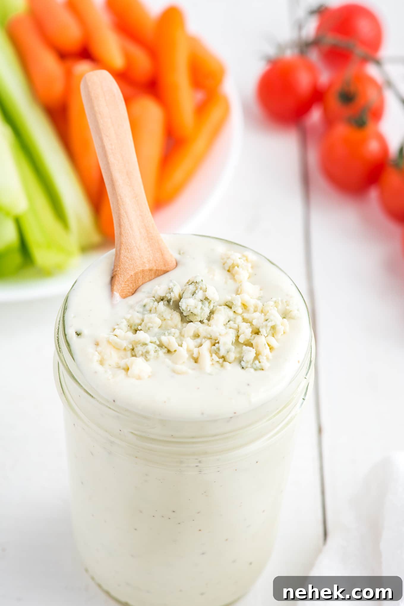 A jar of blue cheese crumbles dressing with a spoon in the jar in front of a platter of veggies.