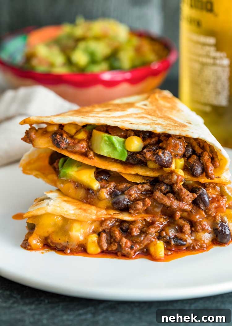 My Crispy Ground Beef Quesadillas are filled with melted Queso quesadilla, cheddar or Monterey Jack cheese, seasoned ground beef, avocado, beans and corn. stacked crispy ground beef quesadillas on white plate with guacamole
