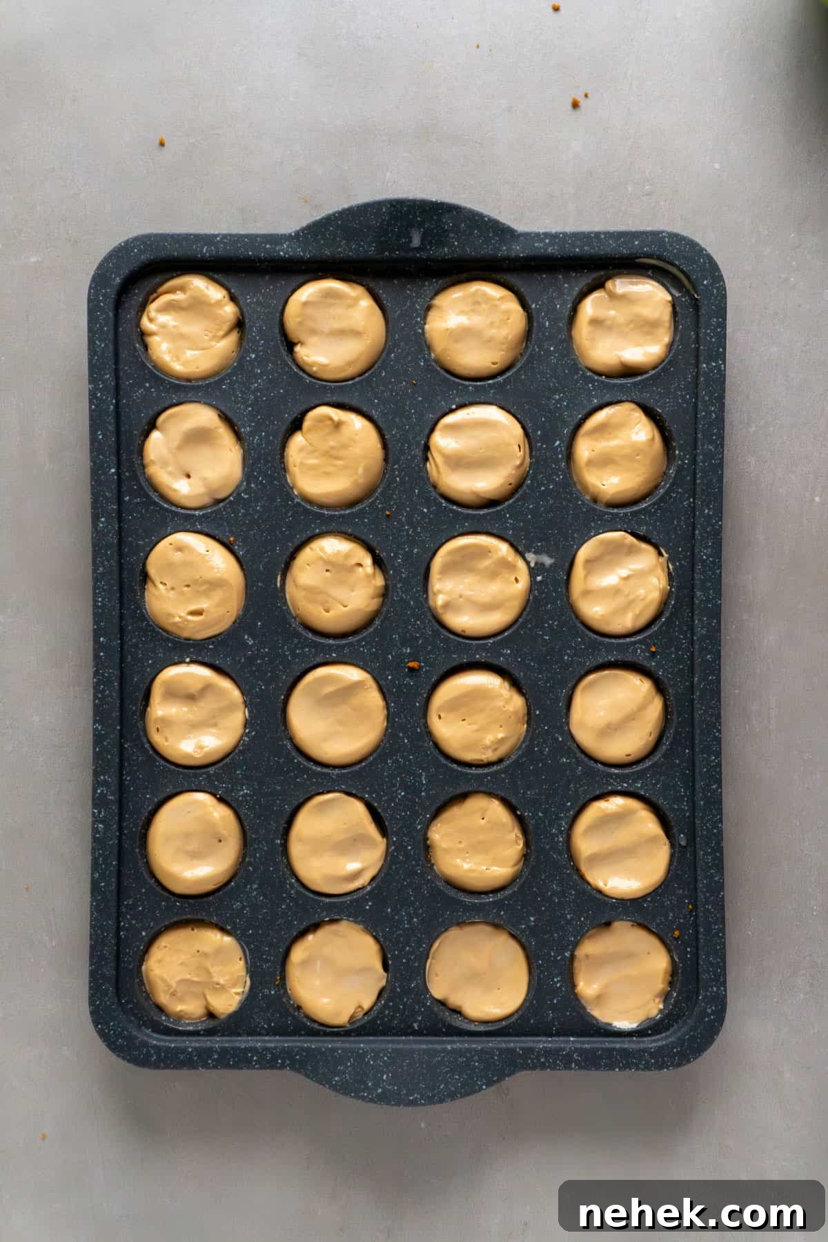 Mini biscoff cheesecakes in a mini muffin pan getting ready to freeze.