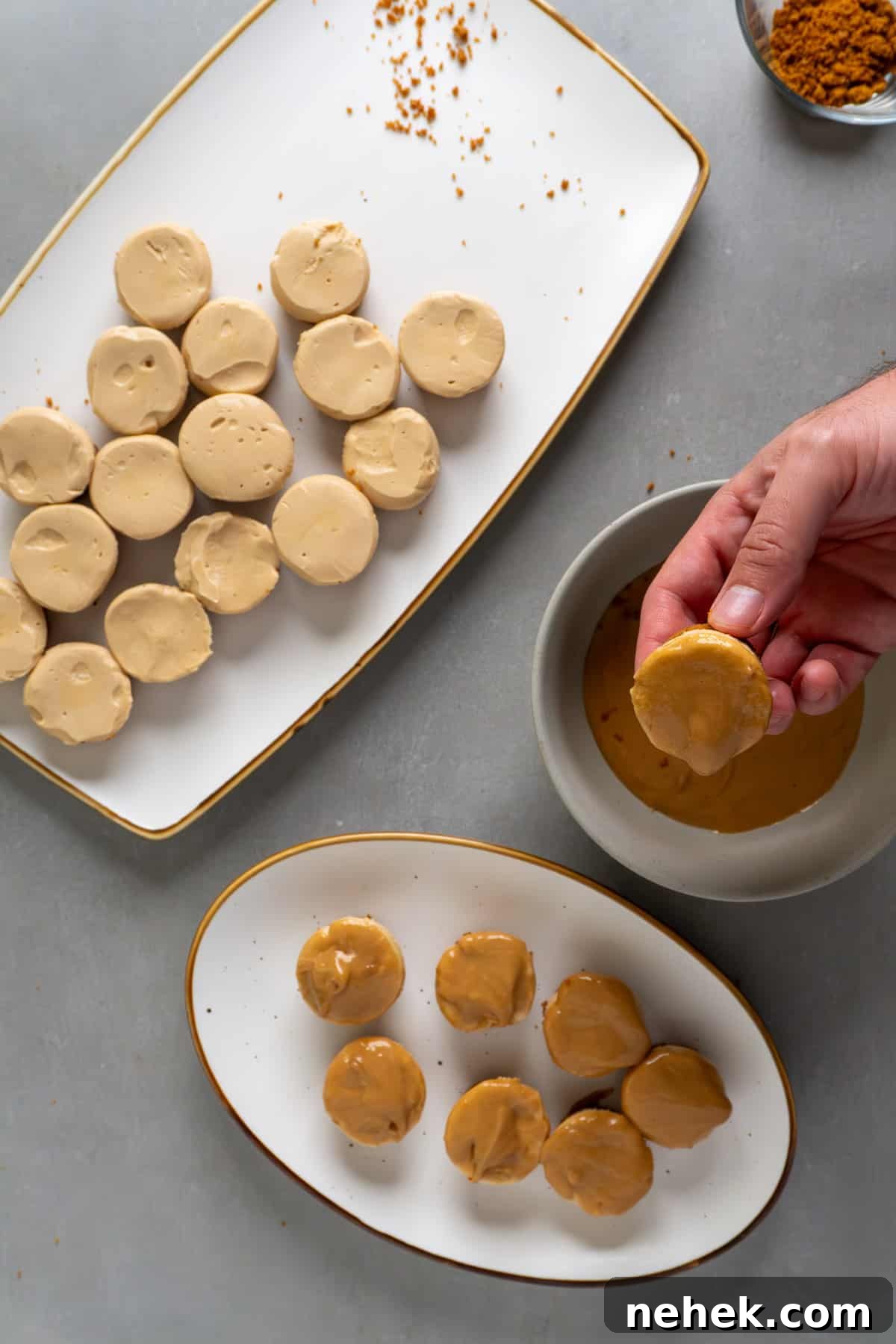 A hand dipping a biscoff mini cheesecake into a cookie butter topping.