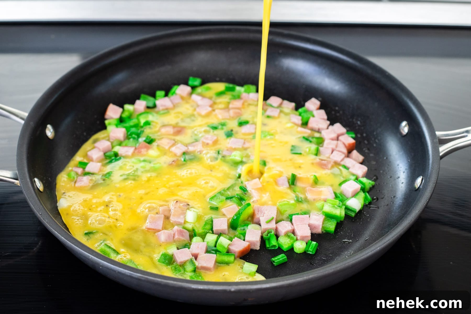 How to Make a Classic Western Sandwich (Ham, Egg & Peppers) 5 Pouring beaten egg over sautéed ham and veggies.