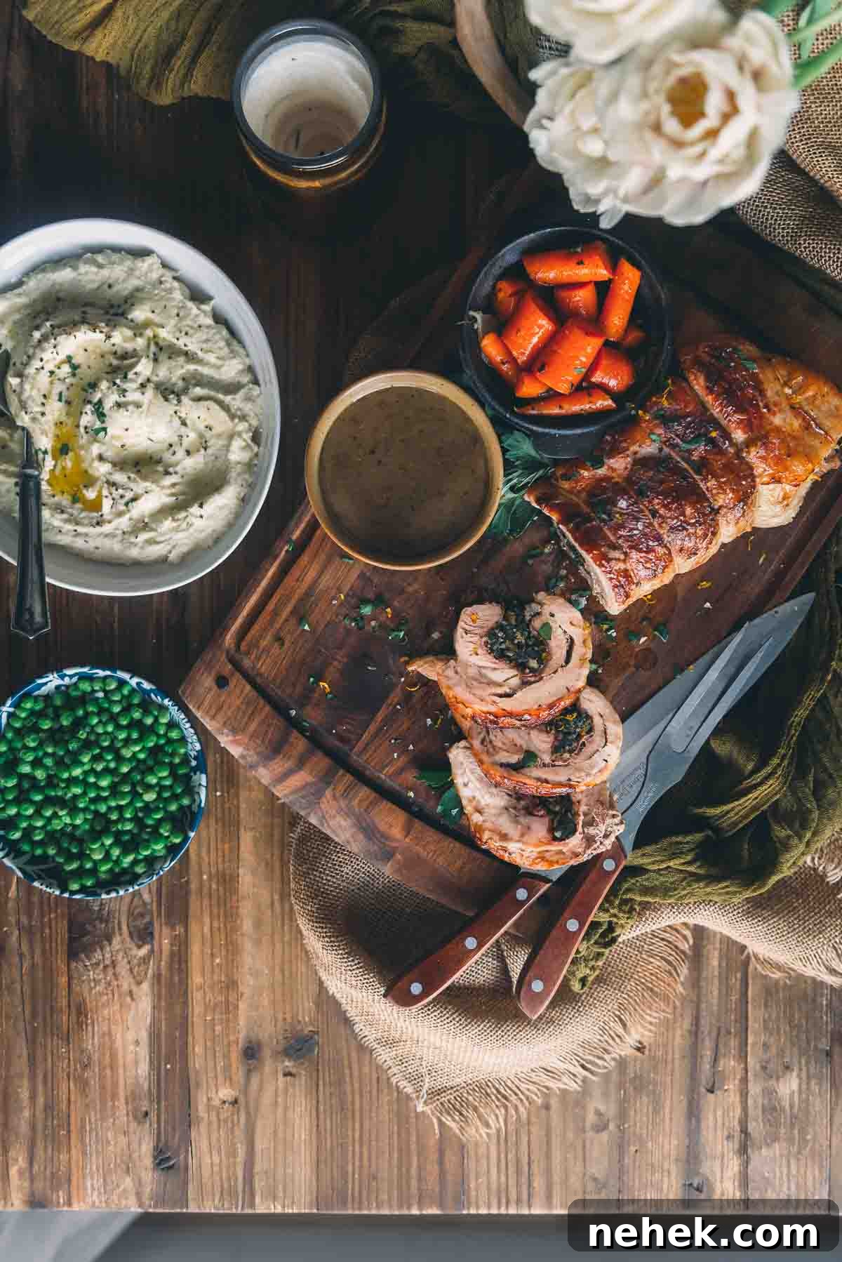 Overhead of roasted veal dinner with side dishes like carrots, peas and mashed parsnips.