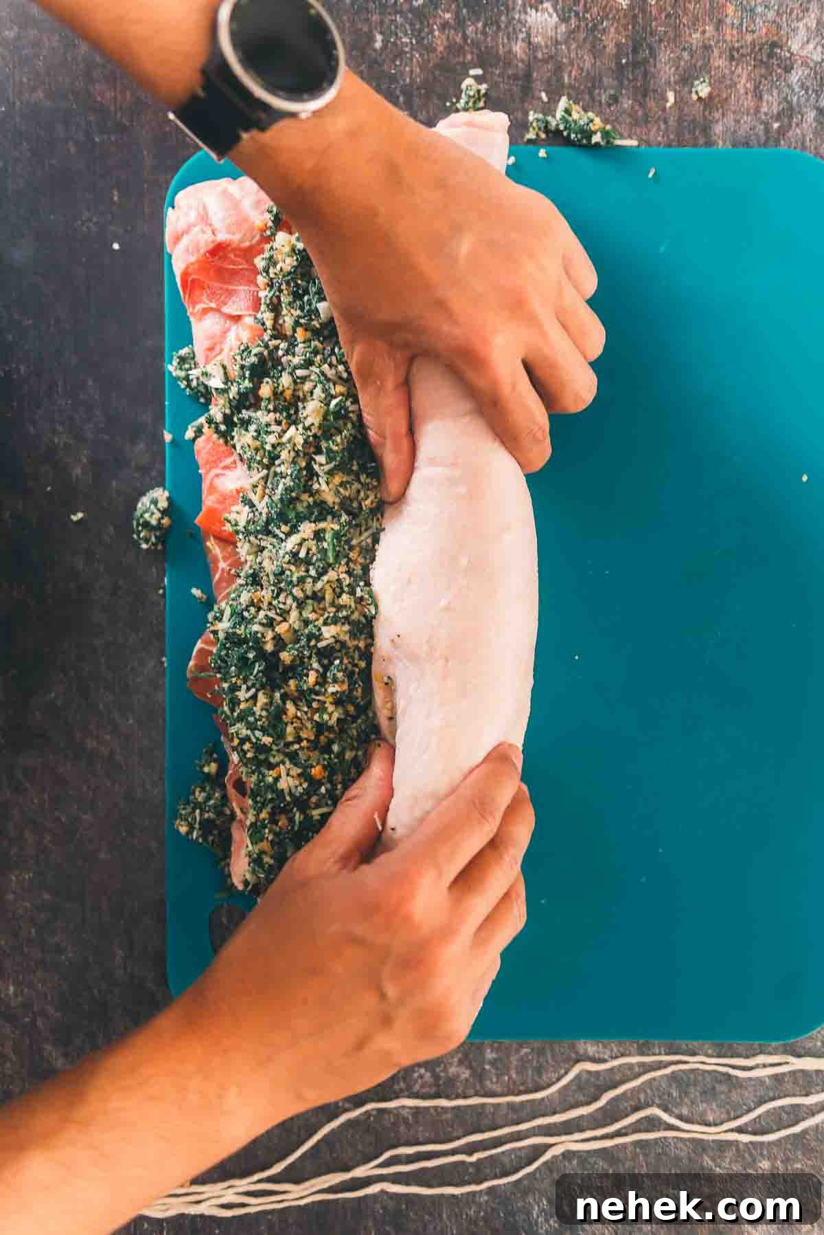 Hands rolling the roast with the stuffing inside.