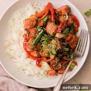 an overhead view of a white plate filled with white rice and salmon stir fry with a silver fork resting on the side of the plate