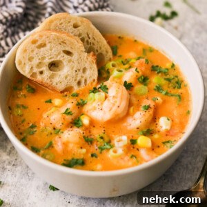 side view of a bowl of soup topped with garnishes and shrimp and two slices of bread.