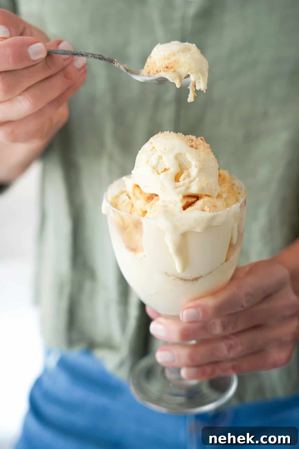 Person with green shirt holding glass of cheesecake ice cream and spooning it.
