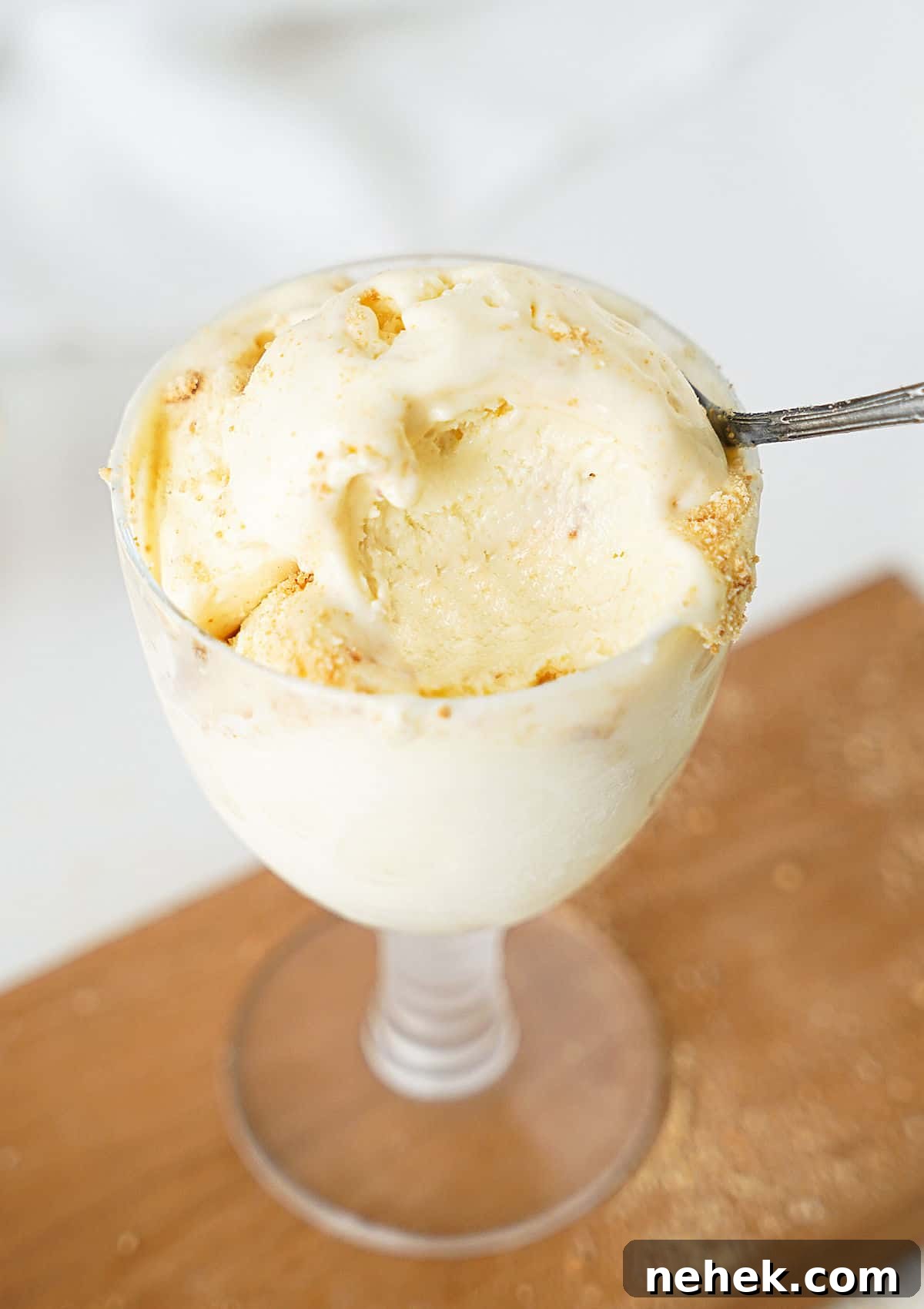 Eaten cream cheese ice cream scoops in a glass on a wooden board. Greyish background. 
