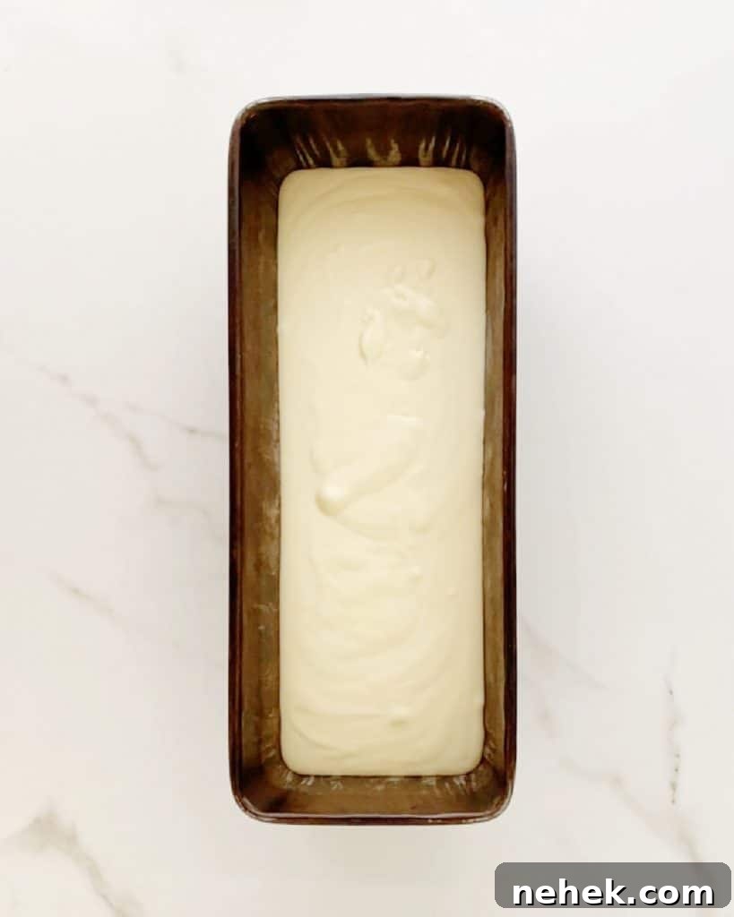 Dark loaf pan with ice crema mixture on a white marbled surface.