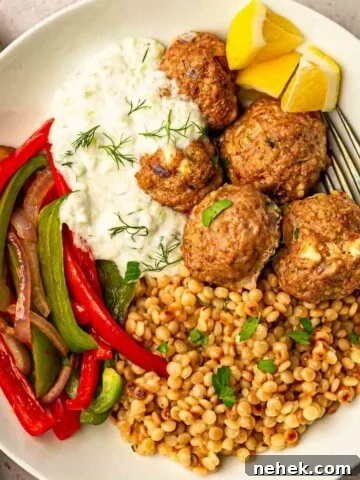 A white plate of Greek meatballs with couscous and red peppers topped with parsley and dill.