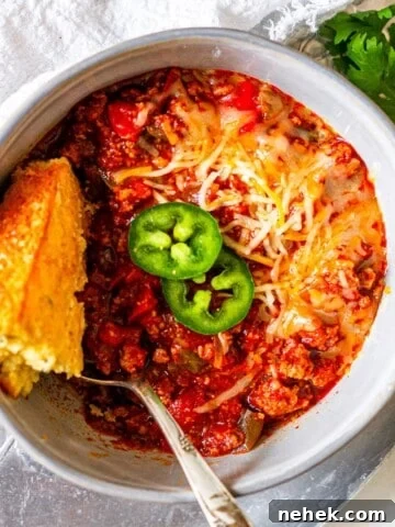 A bowl of chili topped with jalapeno slices and a piece of cornbread.