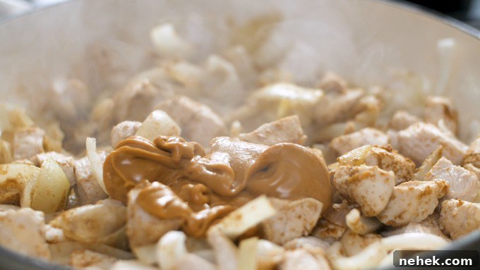 Pan of chicken and onion cooking. Scoop of peanut butter has just been added on top of chicken.