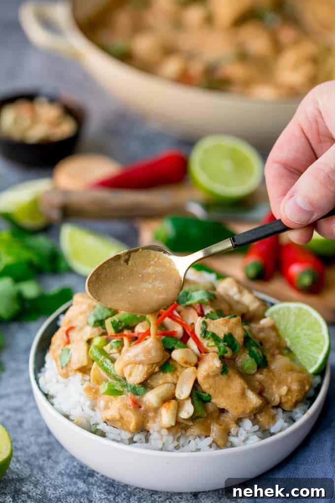 Bowl of rice topped with peanut butter chicken with green beans, chillies and coriander (cilantro). Extra sauce being spooned on top.