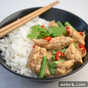 Black bowl filled with rice and peanut butter chicken curry with green beans. Chillies and coriander on top.