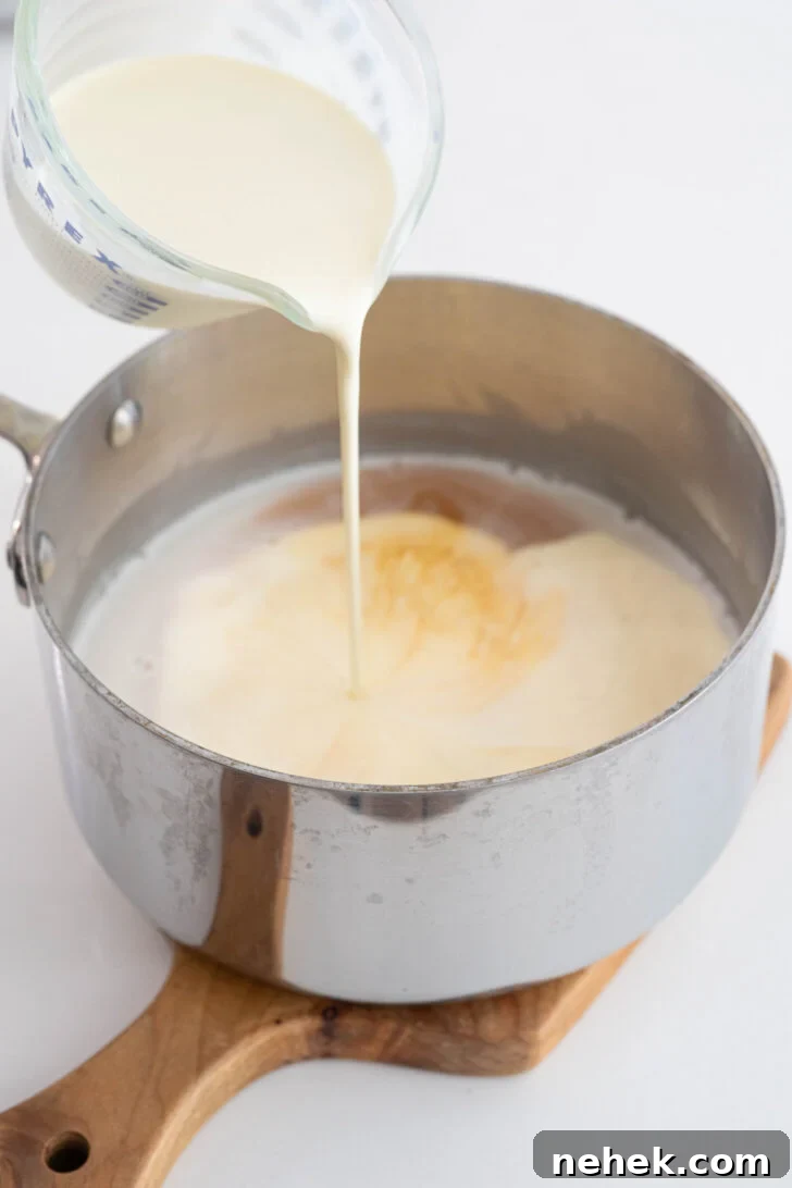 Heavy cream pouring into a pot of coconut milk.
